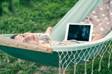 Girl eating chips drinking beer watching a movie on a tablet. Swinging on a hammock.