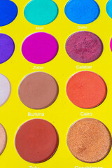 close up and top view of an eye shadow palette of many colors on a yellow background