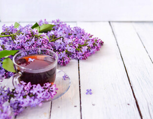 Obraz na płótnie Canvas Cup of tea with lilac flowers on a wooden white background. Mocap for postcards. Spring time. Vase with lilacs. Copy space for text. The concept of holidays and good morning wishes