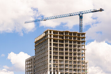 Fototapeta na wymiar Modern monolithic construction of houses against the blue sky. Single construction tower crane during the construction of a monolithic apartment building