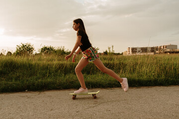 11 year old girl in shorts skateboarding at sunset on the street.