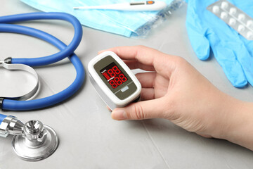 Woman holding fingertip pulse oximeter near medical items at light grey stone table, closeup