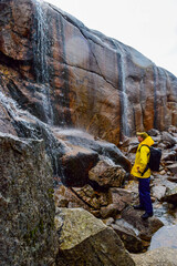 Tourist man looks at waterfalls falling from cliffs near trail to the Kjeragbolten is the most dangerous stone in the world.  Norway.