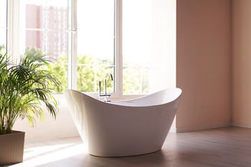 Fototapeta na wymiar Modern bathroom. White bath with green palm branches. Bright room with sunlight from a large window