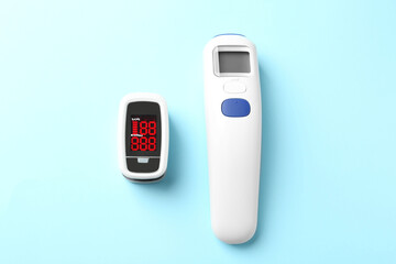 Modern fingertip pulse oximeter and non contact infrared thermometer on light blue background, flat lay