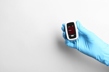 Doctor in gloves holding fingertip pulse oximeter on white background, closeup. Space for text