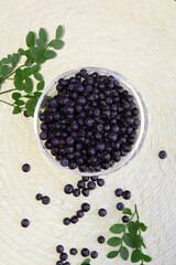 forest Northern blueberry lies in a transparent plate on a round light wicker background, other berries are scattered on the table