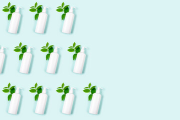 White bottles of antiseptic to protect against germs on pastel blue background. Hygienic product with green leaves, virus concept. Antibacterial pattern. Liquid soap, skin care. Place text. Copy space