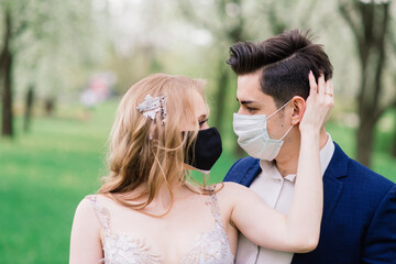 Young loving couple walking in medical masks in the park during quarantine on their wedding day. Coronavirus, disease, protection, sick, illness flu europe celebration canceled.