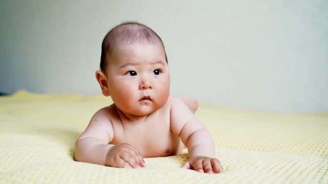 a small newborn Asian baby lies on his stomach and puts his hands in his mouth. teething