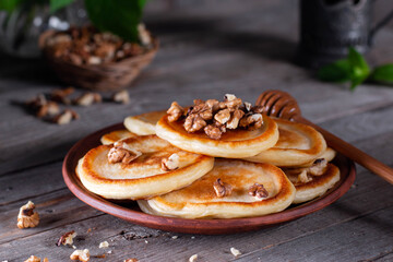 Homemade pancakes with nuts and honey in a ceramic plate on an old wooden table