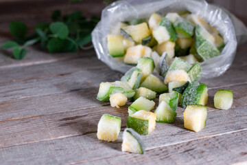 Frozen cubes of zucchini in a plastic bag on the wooden background