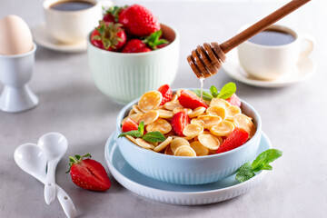 Trendy food - pancake cereal. Honey dripping on heap of mini cereal pancakes in bowl on gray background