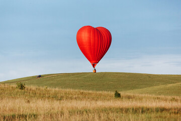 Hot air balloon in shape of heart is landing on the green field