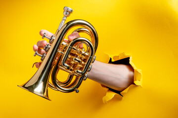 Hand playing a pocket trumpet through torn yellow paper background