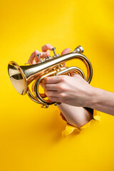 Hands playing on a trumpet through torn yellow paper background