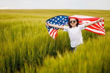 Carefree pretty girl running and smiling on the green field with a blowing flag of USA