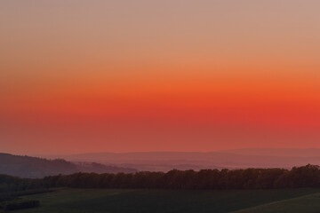 The setting sun over the forested mountain landscape of the Beskydy region, the sun sets beyond the horizon.