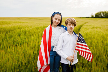 Handsome guy and girl standing in a field with an American flag in their hands