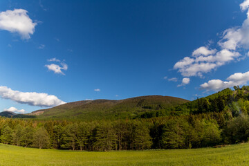 Mountainous landscape and Radhost hill during a sunny day with clouds in the sky.