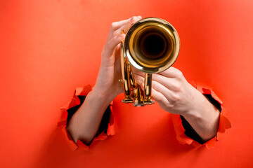 Hands playing trumpet through torn holes in red paper background
