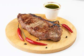 A large piece of meat lies on a board with red pepper isolate