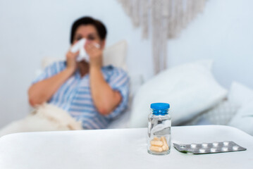 foreground of a tablet in a jar and in a blister. in the background a blurred adult old woman lies...