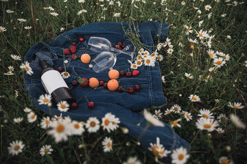a bottle of wine, two glasses, cherries, strawberries on a denim jacket in a chamomile field