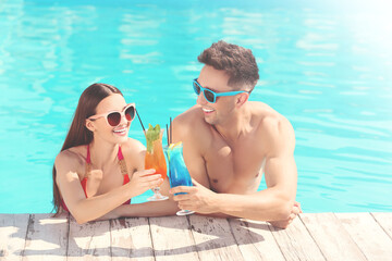 Happy young couple with cocktails in swimming pool