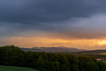 A field of wheat and a view of dark clouds on a hilly landscape before sunset in the distance you can see the rain.