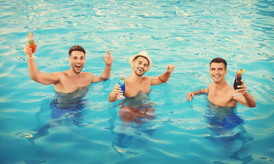 Happy young friends with refreshing cocktails in swimming pool