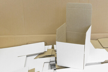 Open cardboard box. A lot of packaging for mugs. Disassembled condition, not folded. Wholesale and retail trade. White color outside, brown inside. Production of souvenirs. Side view.