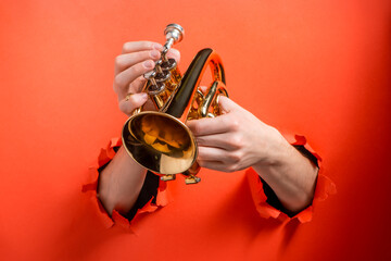 Hands playing trumpet through torn holes in red paper background