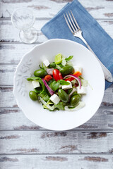 Salad with Green Olives, Cucumber Cherry Tomatoes and Feta Cheese on bright wooden Background. Healthy Snack Idea. Top view. Copy space.