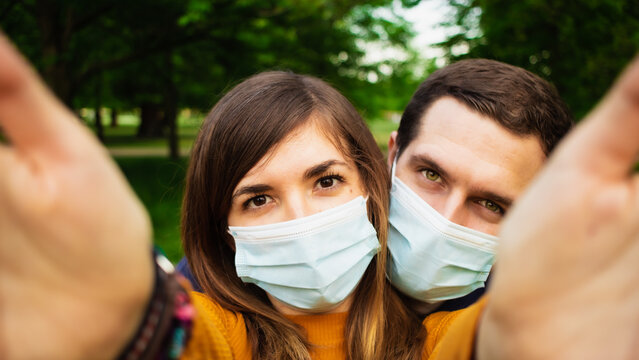 Attractive young couple taking a selfie in a park while wearing face masks due to coronavirus outbreak