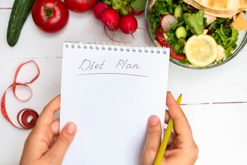 Top view of woman hands holding notepad with handwritten words Diet Plan above white table with...
