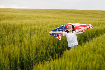 Carefree pretty girl running and smiling on the green field with a blowing flag of USA