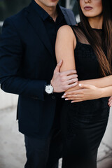 A beautiful, stylish pair of young people in black clothes and glasses stand against the background of an office building in the sunset. Fashion and style