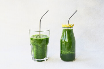 Green smoothie with spinach in small bottle and in drinking glass with metal straw. Copy space. Healthy lifestyle concept