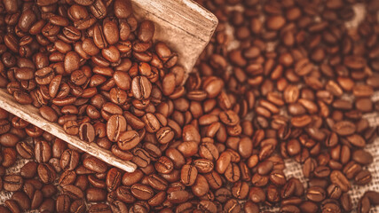 Natural background of scattered roasted coffee beans closeup in a wooden scoop, top view, selective focus, service