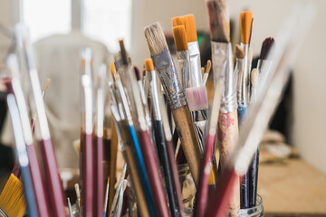 Set of various multi colored artists paintbrushes locating in glass on wooden table of modern art workshop on sunny day