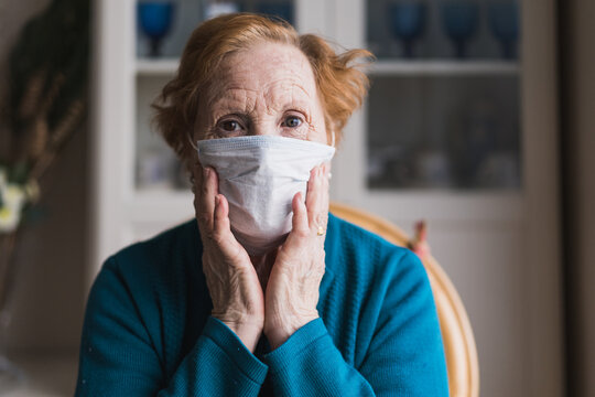 Senior female with red hair in blue robe and medical mask looking at camera while standing in hospital room