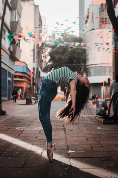 Happy female in casual clothes doing back bend while dancing on the street amidst buildings on modern city