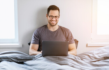 Man With Laptop Working Online Sitting In Bed At Home