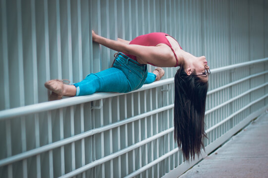 Side view of slip woman in casual clothes and glasses doing splits on fence and bending back while dancing on street