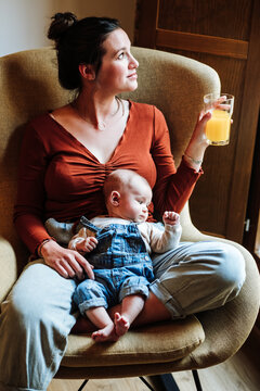 Crop mother with juice and baby resting on chair