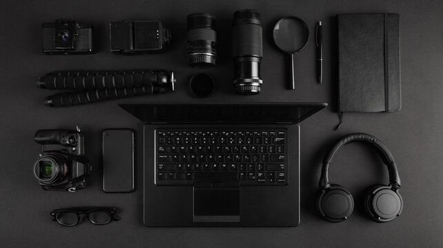 Top view of black modern photography equipment and laptop arranged on dark table.