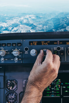 Back view of crop anonymous male pilot turning switch on control panel in cockpit during flight over rocky terrain