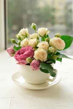 A bouquet of white roses in a cup on a white table opposite the window.