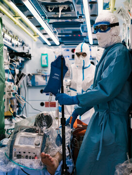 Group of professional doctors in protective uniform standing in ambulance car with equipment and preparing for patient transportation